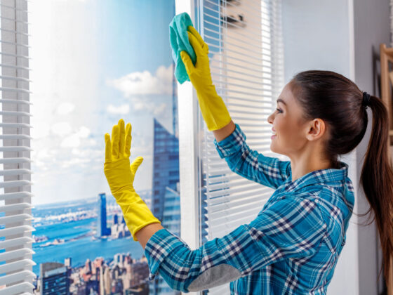 Kobieta w niebieskiej koszuli w kratę i żółtych rękawiczkach myje okna w domu